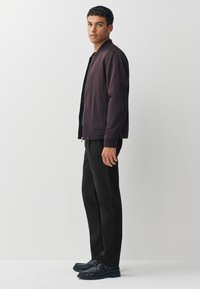 Veste bomber marron foncé avec fermeture éclair à l'avant, pantalon noir et chaussures noires. La veste présente des poignets côtelés et un design épuré.