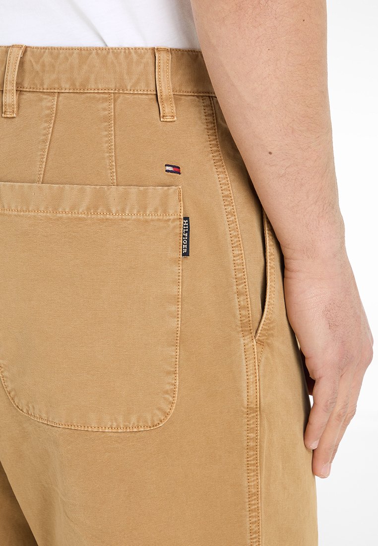 Pantaloni khaki con una texture liscia, dotati di una grande tasca posteriore, etichetta con marchio e piccolo accento del logo nei colori rosso, bianco e blu.