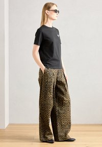 T-shirt nero a maniche corte, abbinato a pantaloni larghi con stampa leopardata in marrone e nero, indossato con scarpe nere a punta e occhiali da sole.