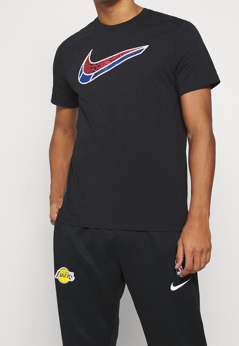 Camiseta negra de Nike con un logo de swoosh colorido y estampado; combinada con pantalones deportivos negros que presentan un logo de los Lakers. Textura suave, diseño de cuello redondo.