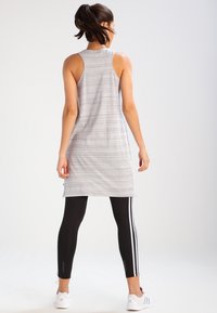 Top sportivo grigio con design a schiena scoperta, abbinato a leggings neri con strisce bianche lungo i fianchi.