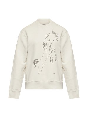 Persona che indossa una felpa color crema con un'illustrazione di un cavallo e pantaloni larghi color ruggine con scarpe basse beige, in piedi davanti a uno sfondo bianco.