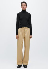 Czarny golf dopasowany, w połączeniu z beżowymi spodniami z wysokim stanem i plisami, zakończony czarnymi butami. Styl minimalistyczny.