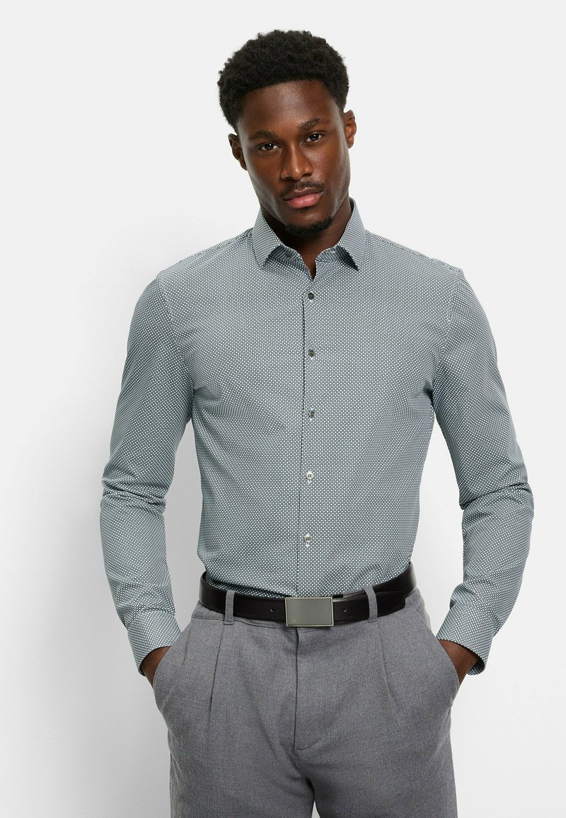 Hemd in Hellblau mit Muster, Kragen und Knopfverschluss, verziert mit kleinen geometrischen Formen, kombiniert mit grauen Hosen und einem schwarzen Gürtel.