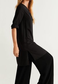 Tunique noire avec un col en V, des manches trois-quarts et des fentes sur les côtés. Tissu doux et coupe décontractée, assortie à un pantalon noir large.