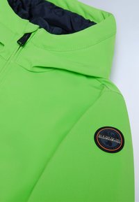 Giacca con cappuccio verde realizzata in un materiale liscio e elastico. Presenta un patch circolare con il logo sulla manica e una cerniera nera.