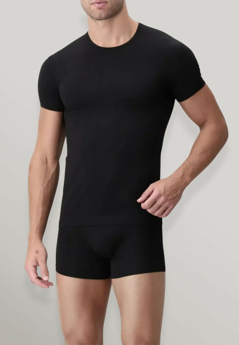 T-shirt nera aderente in tessuto elastico con scollatura a girocollo e maniche corte, abbinata a pantaloni boxer aderenti dello stesso colore.