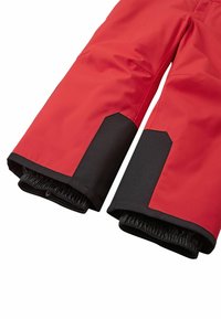 Röda vattentäta snöbyxor med svarta elastiska muddarna och förstärkta nederkanter. Har en slät yta och slitstarka sömmar.