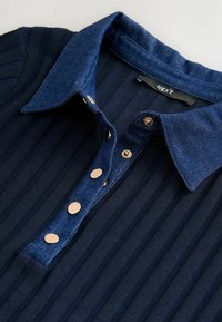 Gros plan sur une chemise en tissu côtelé bleu marine avec un col en denim bleu foncé et des boutons pression dorés le long de la patte de boutonnage.