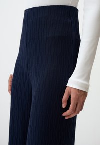 Pantaloni larghi a righe blu navy in tessuto testurizzato, presentati insieme a un top bianco attillato a maniche lunghe con costine, che mostra un primo piano della vita.