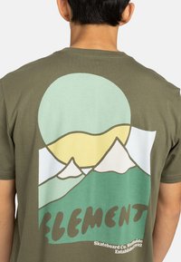 Olivegrünes Baumwoll-T-Shirt mit einem Grafikdesign von Bergen, einer Sonne und dem Wort "ELEMENT" in fetten Buchstaben. Glatte Textur, lässige Passform.