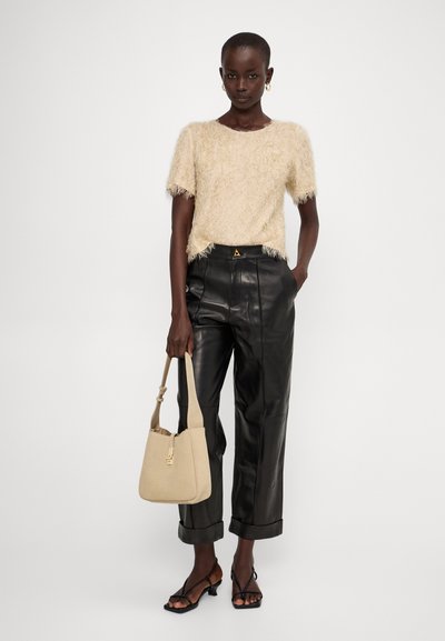 Top beige corto e peloso a maniche corte, pantaloni in pelle neri a vita alta, borsa a spalla beige e sandali neri con cinturini e tacco quadrato.