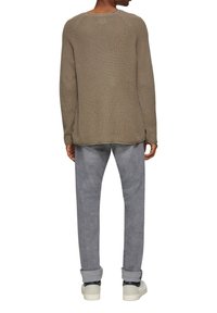 Pull en tricot beige avec des manches raglan, coupe décontractée et tissu texturé. Associé à un pantalon gris clair et des baskets blanches.