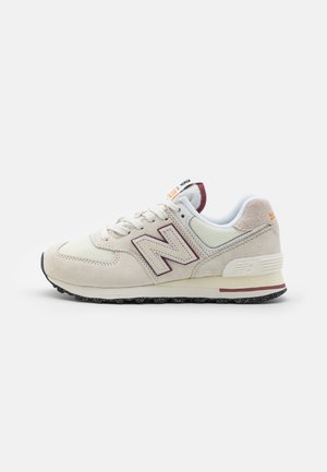 Beżowo-biały sneaker New Balance z bordowymi akcentami logo, białymi sznurowadłami, wyściełaną podeszwą i teksturowaną czarną podeszwą zewnętrzną na jednolitym tle.