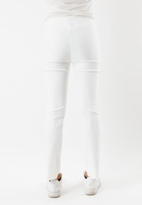 Pantaloni bianchi aderenti con una texture liscia e una silhouette snella. Presentano un piccolo spacco in fondo e sono abbinati a sneaker bianche.