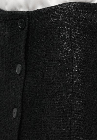 Tessuto nero texturizzato con una leggera lucentezza e motivo della trama visibile. Presenta quattro bottoni neri lungo la parte anteriore per la chiusura.