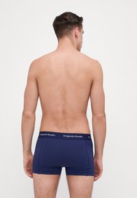Marineblauwe boxershorts met een gladde textuur en een elastische tailleband gelabeld "Originals Studio," getoond vanaf de achterkant op een blote torso.