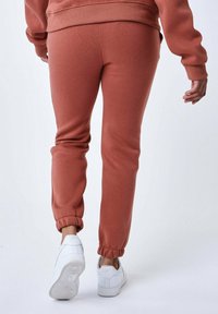 Joggers color rojo ladrillo en material suave, con puños en los tobillos gathered, combinados con zapatillas blancas. El diseño ofrece un ajuste relajado.