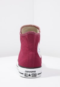 Sneaker montante en toile bordeaux avec semelle en caoutchouc blanche et bande noire, dotée d'un patch de logo rond et d'un col contrasté en piqûre.