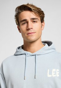 Felpa leggera blu con cappuccio regolabile, caratterizzata da un logo bianco "LEE" sul davanti e punte metalliche sui lacci.