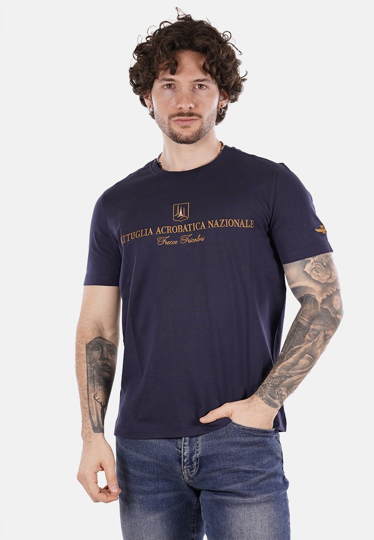 T-shirt in cotone blu navy con collo rotondo, maniche corte e testo e logo stampati in oro. Presenta un design aderente e una texture liscia.