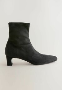 Bottine en daim noir avec un bout pointu, un talon modéré et une finition lisse. Présente des détails de couture sur les côtés.