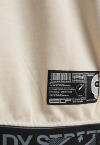 Beige tkanina s černobílou etiketou, na které je nápis "Extremní pohodlí a flexibilita" a vícejazyčný text o výkonu a vášni.