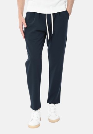 Pantaloni tapered blu navy con vita elastica e cordino, dotati di due tasche laterali, abbinati a sneaker bianche con suola in gomma.