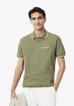 Polo shirt verde oliva in un materiale morbido, con colletto bianco e dettagli delle maniche, e una piccola tasca sul petto con dettaglio del logo.