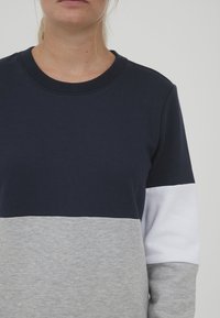 Tengerészkék, szürke és fehér színblokkokból készült pulóver, kerek nyakkivágással és hosszú ujjakra, puha pamut anyagból.