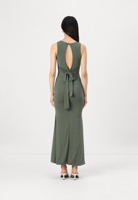Robe longue vert olive avec un dos en trou de serrure, un détail noué à la taille et une fente sur le côté. Tissu lisse avec une silhouette ajustée et un design longueur sol.