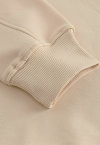 Beige sweatshirt manchette gemaakt van zacht, ribbelstof met een nette afwerking. Naaddetails zichtbaar langs de rand. Over het algemeen een gladde textuur.