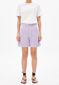 Světle levandulové džíny šortky s vysokým pasem, předními kapsami a ohrnutým lemem, v kombinaci s jednoduchým bílým tričkem a černými sandály na pásky.