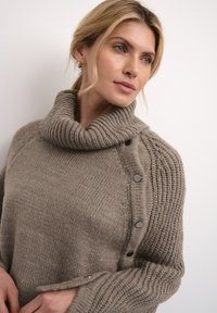 Paksu kudumine, taupe värv, üle mõõdu suuruse kaelus, ribade muster varrukatel, külgedel nupud ja pehme tekstuur.