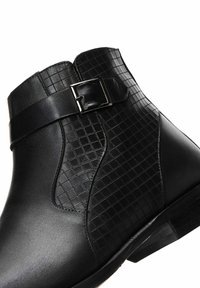 Botas negras hasta el tobillo con un upper de cuero liso y un patrón de cuadrícula texturizado en el lateral, y un detalle de hebilla. Tacón bajo.
