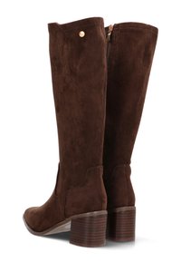 Botas de ante marrón hasta la rodilla con punta redondeada y un tacón de bloque apilado, con una cremallera lateral y un pequeño detalle decorativo de tachuela.
