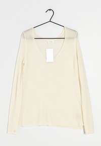 Top a maniche lunghe con scollo a v in morbido materiale crema. Presenta una vestibilità ampia e un orlo dritto. Include un'etichetta appesa dal collo.