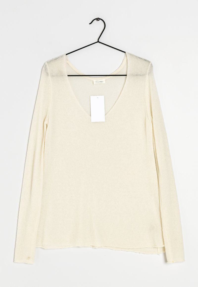 Top a maniche lunghe con scollo a v in morbido materiale crema. Presenta una vestibilità ampia e un orlo dritto. Include un'etichetta appesa dal collo.