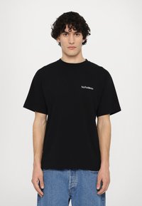 Svart bomulls t-skjorte med korte ermer, rund hals, og hvit "No Problemo" tekst på venstre bryst. Kombinert med blå denimjeans.