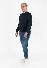 Marine hoodie met ribbels aan de mouwen en onderkant, gecombineerd met lichtblauwe spijkerbroeken en witte sneakers. Eenvoudig ontwerp, van katoen.