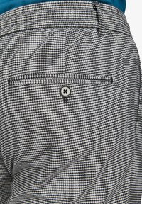 Sort-hvid houndstooth mønster på en bukselomme med en sølvknapdetalje og en ekstra lille lomme ovenfor.