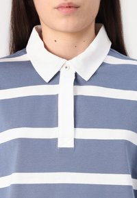 Polo riscado azul e branco com colarinho branco, pala com botões e textura suave e lisa de algodão. Apresenta riscas horizontais.