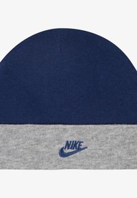 Kniautas kepurė tamsiai mėlynos ir šviesiai pilkos spalvų. Yra perlenkta kraštinė su mėlynu "Nike" logotipu, išsiuvinėtu pilkame skyriuje. Minkšta tekstūra.