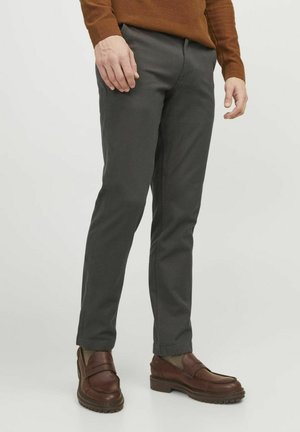Graue, schmal geschnittene Hose aus glattem Stoff, mit einem mittelhohen Bund und seitlichen Taschen, kombiniert mit braunen Mokkasins.