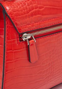 Rote Handtasche aus Kunstleder mit Krokodil-Prägung, ausgestattet mit einem silbernen Metallreißverschluss und kontrastierenden Nähten entlang der Kanten.