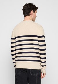Maglione a righe beige e blu navy con texture a coste, colletto girocollo e maniche lunghe. Presenta una vestibilità rilassata e polsi e orlo in tinta unita.