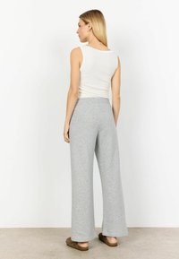 Pantaloni gri, cu talie înaltă și croi larg, dintr-un material moale, având o textură netedă și o talie elastică, asociați cu un top alb fără mâneci.