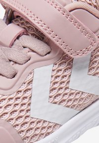 Růžová sportovní bota s prodyšným svrškem, syntetickými akcenty a bílým designem ve tvaru cik-cak. Obsahuje suchý zip a texturované detaily povrchu.