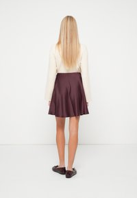 Rövid ujjú krém felső, amely egy bordó selyem szoknyával van párosítva, amelyik flared formájú és sima textúrájú, sötét, lapos cipőkkel viselve.