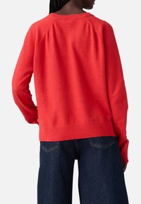 Pull en maille rouge avec une coupe décontractée, des manches raglan et un col rond côtelé, associé à un jean en denim foncé taille haute.